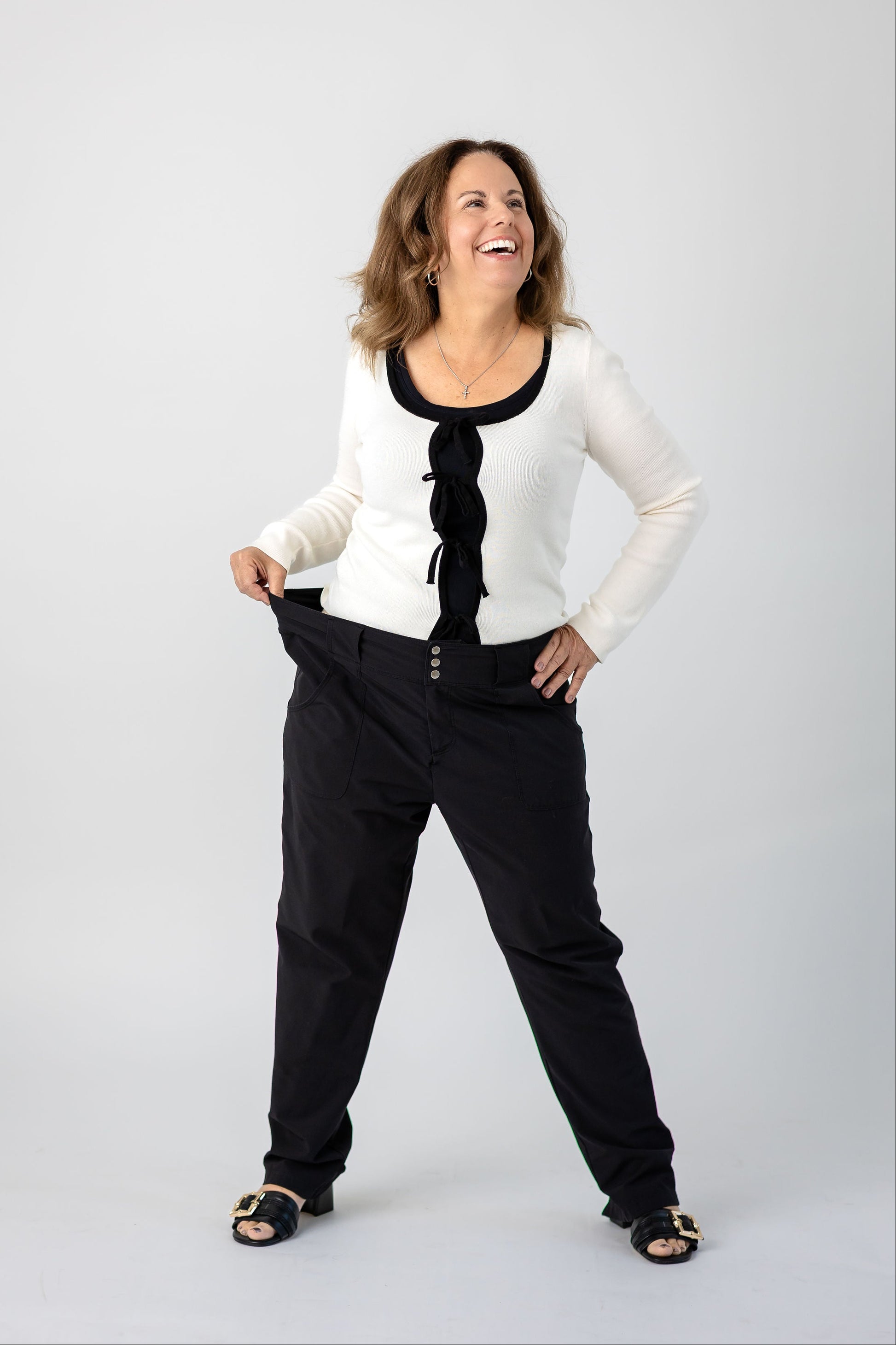 Woman wearing a white cardigan over a black top and black pants on a white background